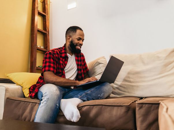 Black man in casual clothes using laptop at home.