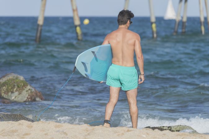 Male surfer with blue board approaching the water