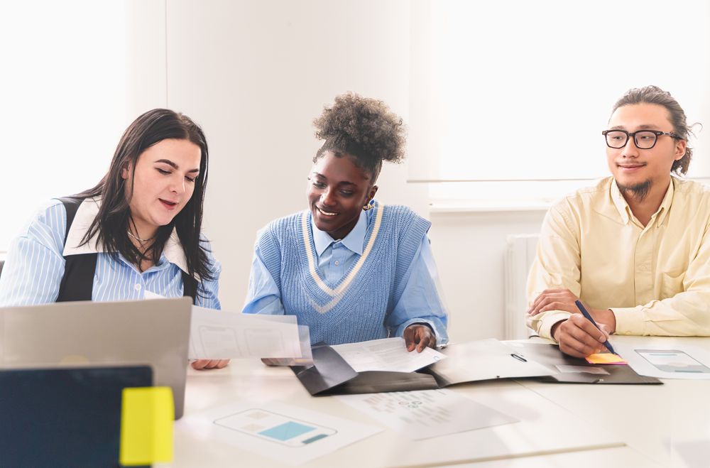 A diverse team of colleagues, including an Asian, Black, and white woman, discussing ideas at a desk