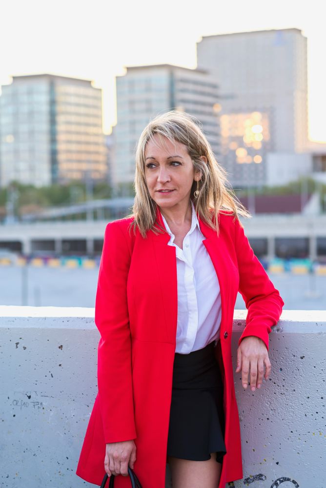 Happy woman in red coat standing on top of building with view of city behind her