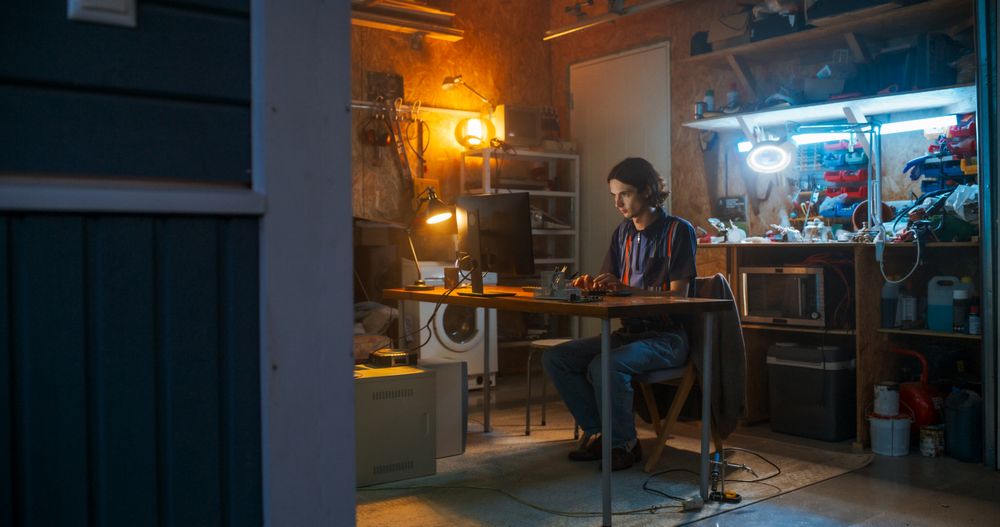 Wide Shot Of White Male Software Engineer Coding on Old Desktop Computer In Retro Garage In The Evening.
