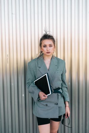 Woman with tablet in stylish suit standing nearby wall holding sunglasses