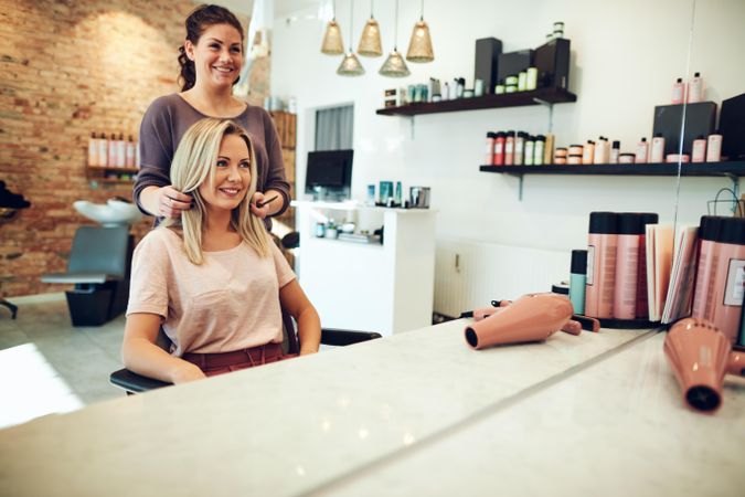 Skilled hairdresser preparing to trim customer’s blonde hair