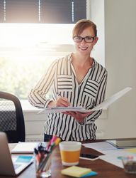 Smiling female in striped shirt looking through binder in her home office, vertical