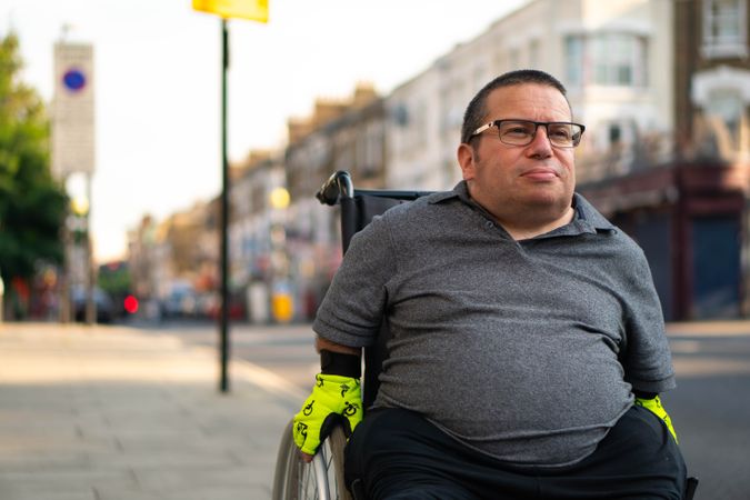 Portrait of man sitting in wheelchair on sidewalk in city