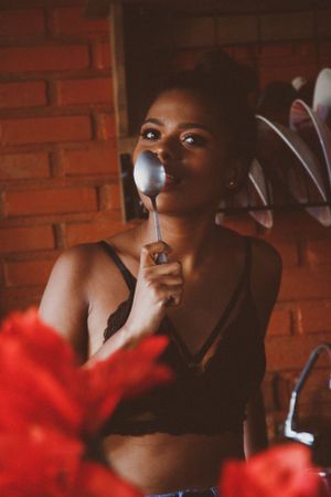 Woman eating with spoon standing near red flowers in the kitchen