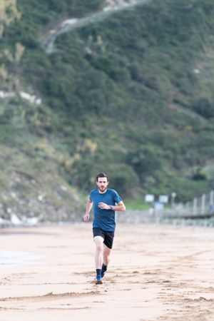 Sportsman in active wear jogging on lonely beach