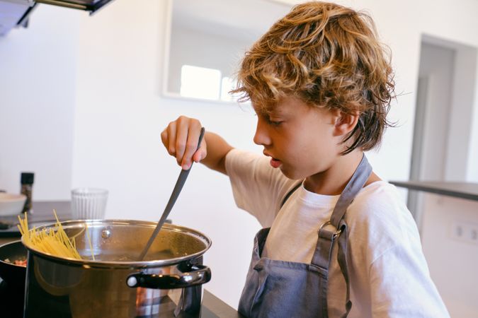 Boy stirring spaghetti in saucepan while cooking at home