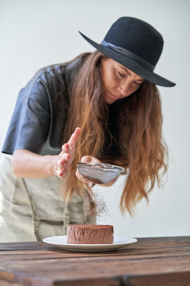 Female sifting chocolate powder through sieve on cake
