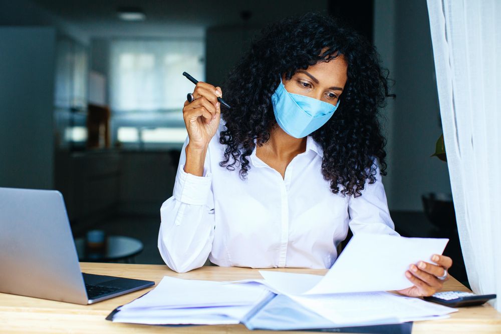 Woman reading over documents with a laptop while wearing a facemask