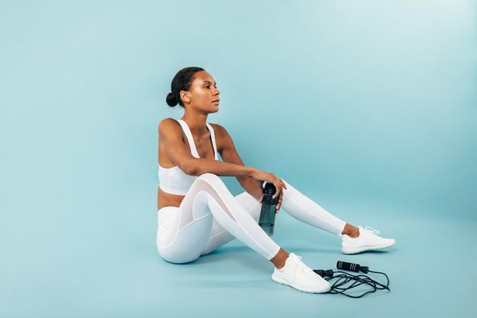 Woman sitting in blue studio after working out with jump rope and water bottle