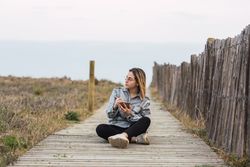 Dreamy woman sitting on boardwalk and writing in notebook in nature