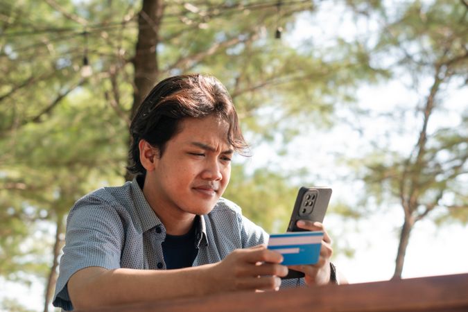 Happy Asian Young businessman hold blue creditcard and phone purchasing online shopping in outdoor cafe.
