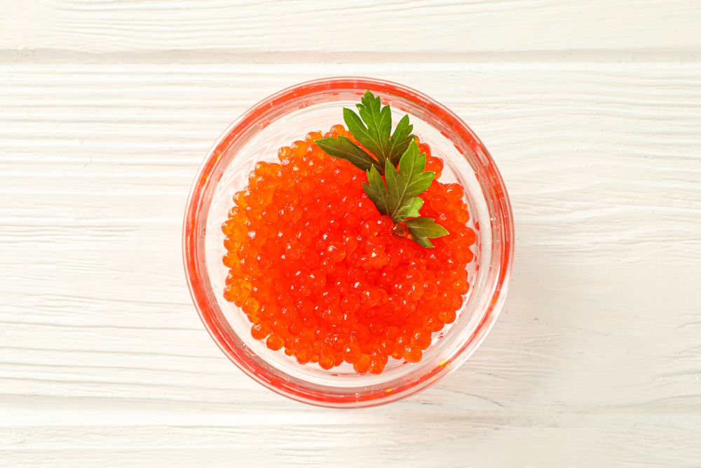 Glass jar with red caviar isolated on wooden table, space for text