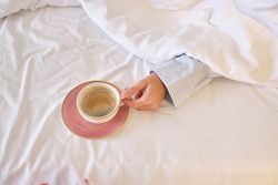 Anonymous female in bed with cup of morning coffee