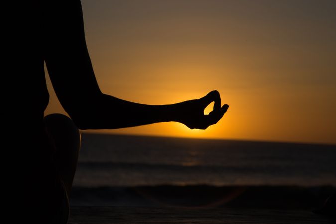 Woman meditating on seashore at sunset