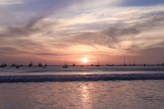 Ships in sea near coast at sunset