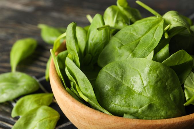 Wooden bowl with spinach and napkin on wooden background