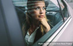 Beautiful young businesswoman sitting on back seat of a car and looking outside the window bGN9V4