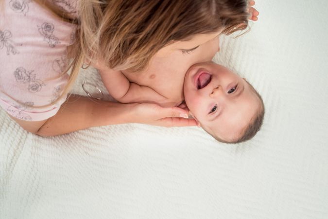 Woman playing with little happy baby on bed