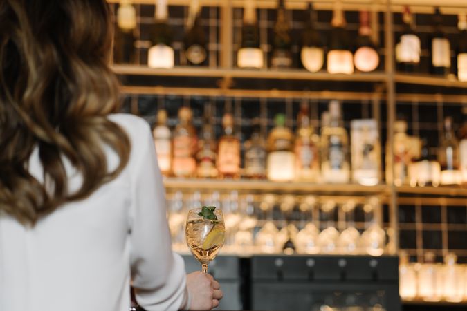 Back view of anonymous woman holding a cocktail in bar