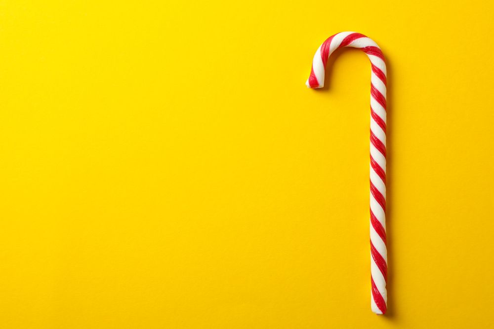 Sweet candy cane on yellow background, space for text