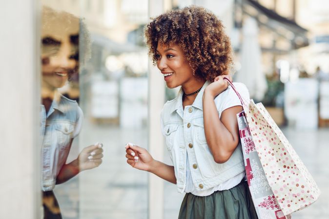 Happy woman standing on street with shopping bags looking at window