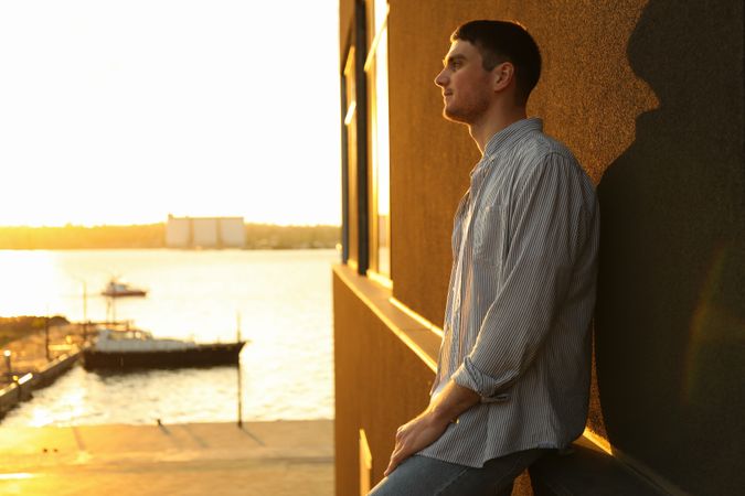 Young man stands leaning against a wall. Amazing sunset