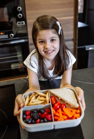 Happy girl showing lunch box filled with healthy food