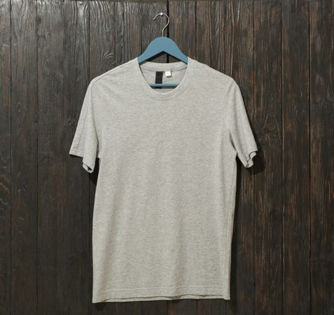 Hanger with blank gray t-shirt on wooden background, space for text