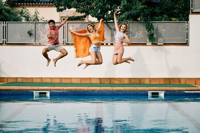 two young women and a man jumping by the pool