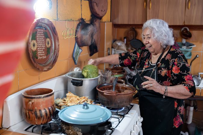 A mature woman is smiling while preparing chayote to go with battered poblano chiles