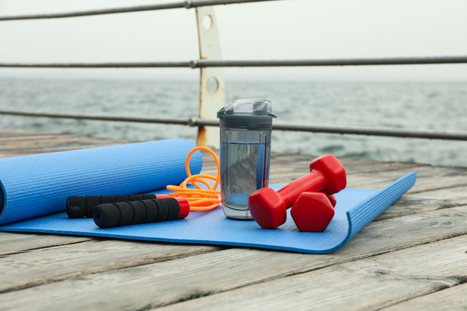 Yoga mat, jump rope, dumbbells and bottle of water on wooden floor outdoors