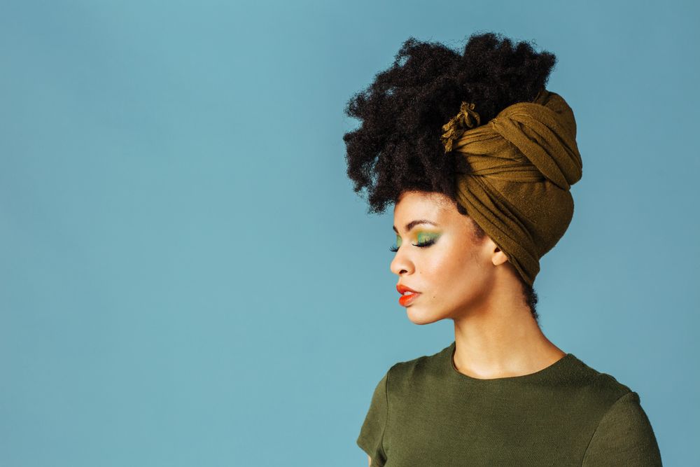Studio shoot of Black woman with her eyes closed wearing a green hair scarf