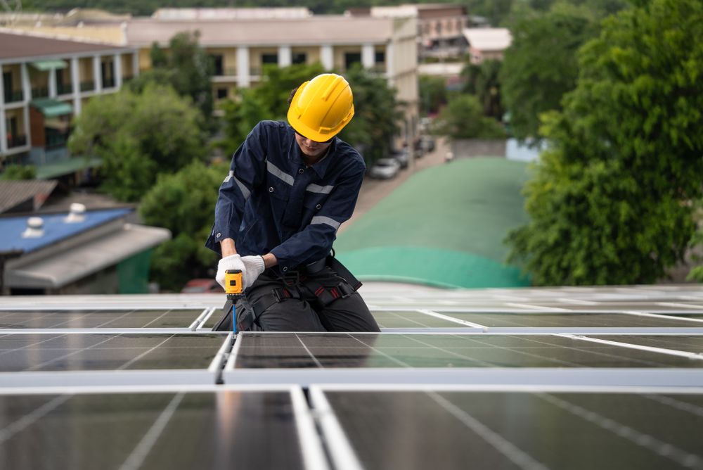 Engineer worker using electric drill repairing on solar cell panel on the roof of the factory. After service and security for industrial renewable energy concept