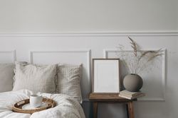 Bedside table with mockup frame and vase next to comfortable bed with tray of coffee