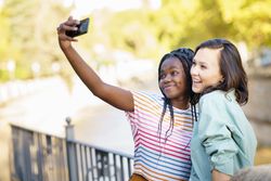 Women friends taking selfie with phone in casual clothing outside
