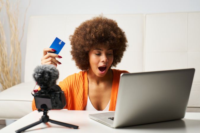 latina woman with afro hair surprised while shopping online with laptop and paying by credit card