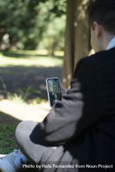 Back view of a young male student sitting on campus while using a mobile phone 5pgkl8