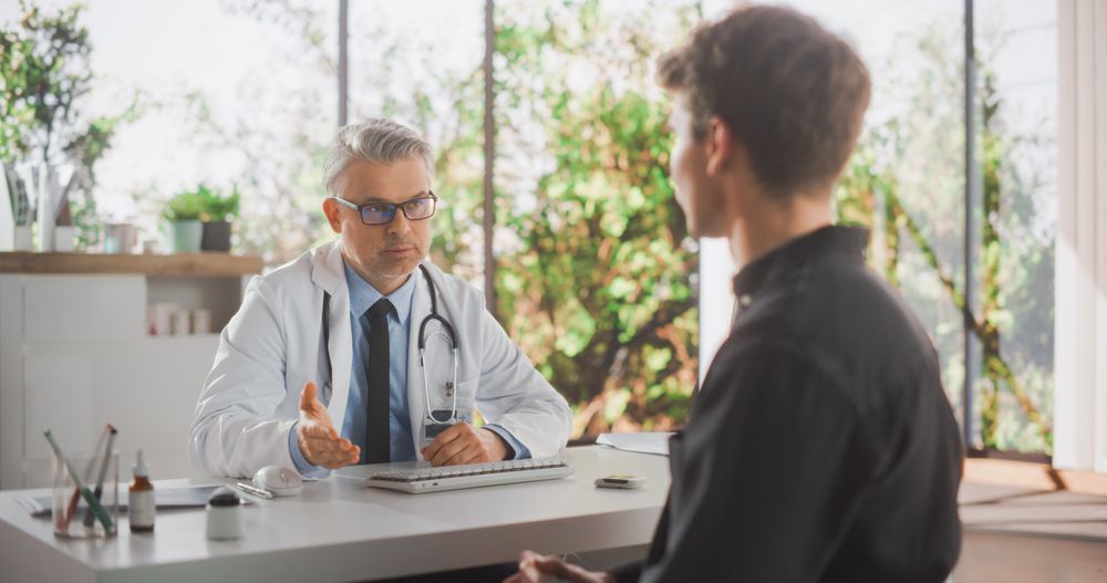 Doctor with Elegant Grey Hair Showing Analysis Results on Tablet Computer to a Healthy Young Man During a Visit to a Private Health Clinic.