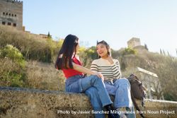 Two female friends sitting on stony wall on nice day in Spain 47Yaz0