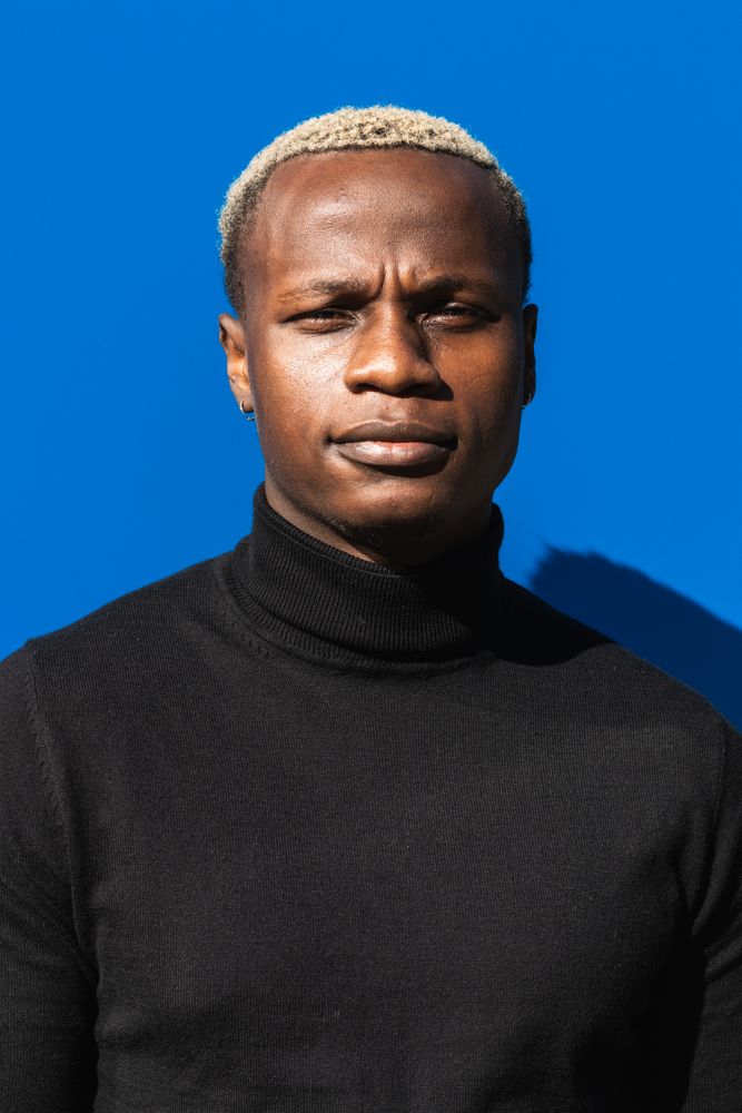 Serious Black guy standing against blue wall in sunlight