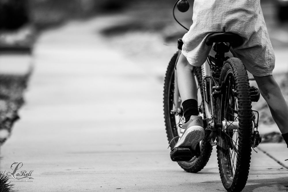 Back view of a boy riding bicycle on road in grayscale