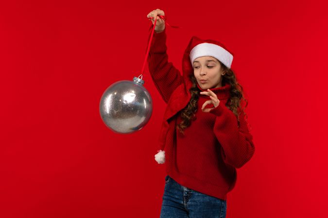 Girl in Santa hat and sweater holds Christmas ornament