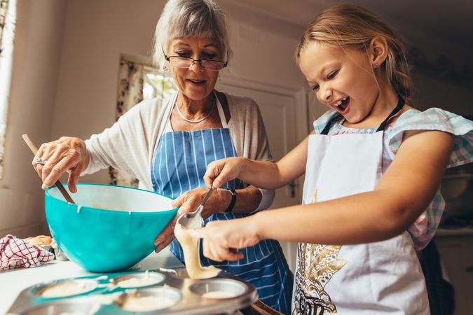 Little girl learning to make cup cakes with grandmother