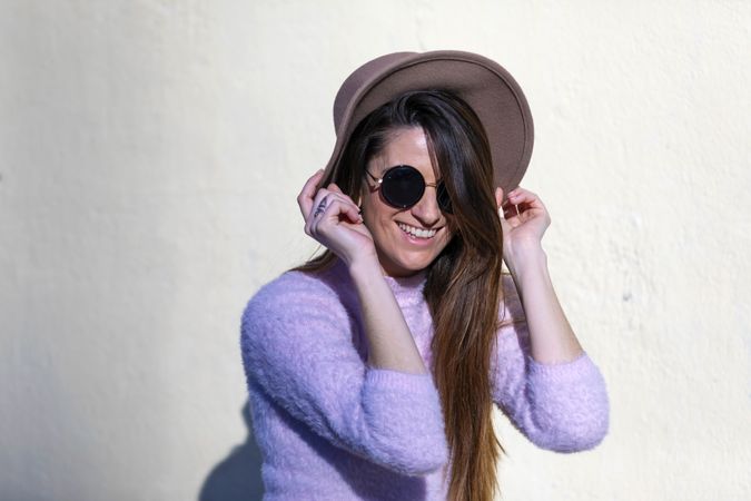 Front view of smiling woman wearing sunglasses and hat standing in a sunny street