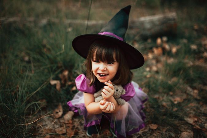 Happy girl in witch costume sitting down in the grass