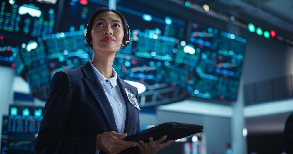 Female Investment Banker Wearing Headphones and Using a Tablet Computer with Financial Market Analytics Data.
