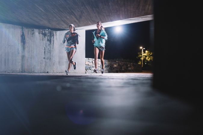 Young women jogging under bridge at night