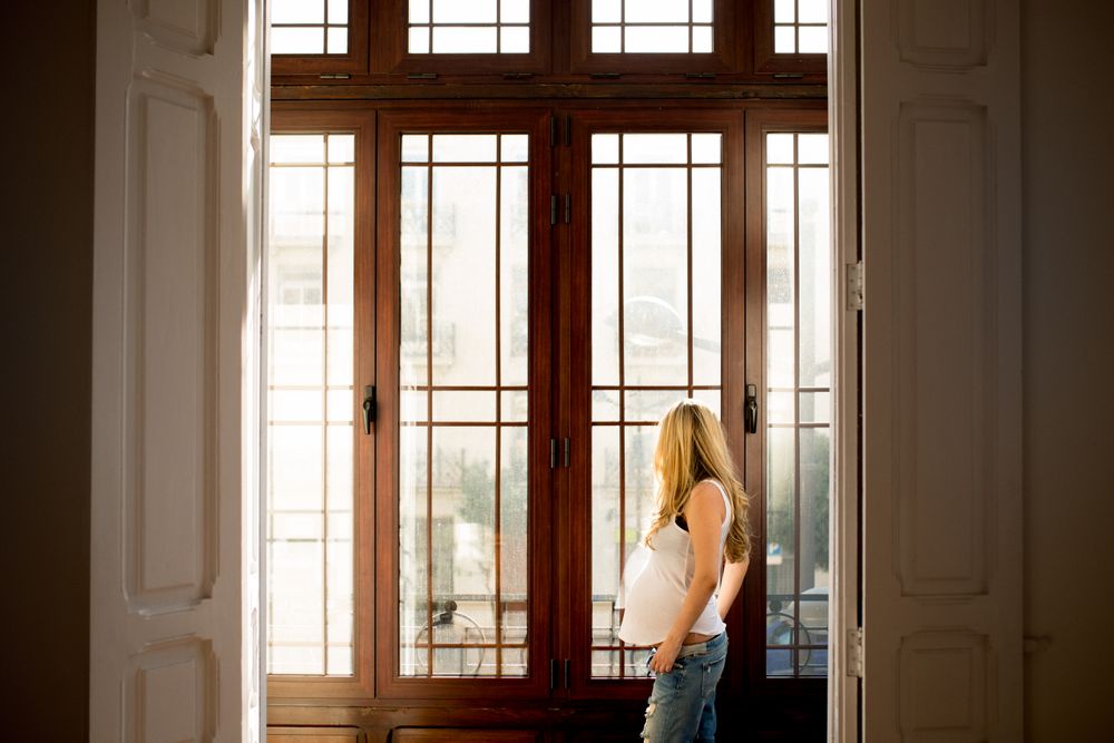 Pregnant woman near open door looking out window